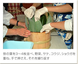 笹の葉を３～４枚並べ、野菜、サケ、コウジ、ショウガを重ね、手で押さえ、それを繰り返す